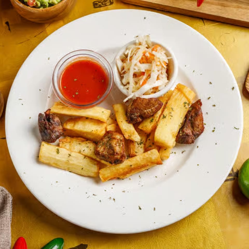 Delicia's Salvadoran yuca frita with fried pork, curtido, and red sauce on a white plate.